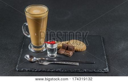 aromatic coffee latte with chocolate chunks and crispy buttered biscuits with a spoon and forks with a glass of vodka and chili pepper whole black stone plate sweet set