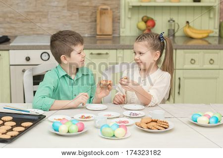 Cute kids baked cookies and tasting it at the table in the home kitchen.
