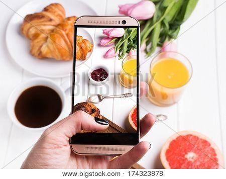 Woman's hand taking photo of delicious breakfst with smartphone close-up
