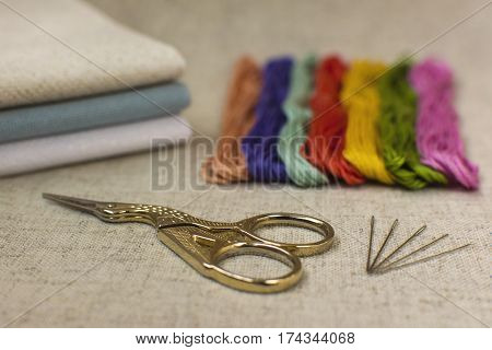 Close-up of the embroidery and cross-stitch kit on a natural linen background. Scissors needles colored threads and canvas.