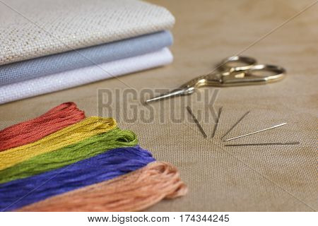 Embroidery and cross-stitch kit on a natural linen background. Focus on the needles.