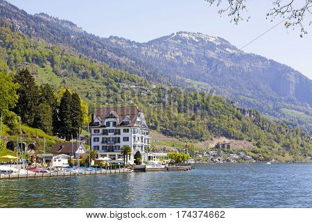 WEGGIS SWITZERLAND - MAY 05 2016: Hotel and a small marina by the Lake Lucerne on the background of mountains creates mood of vacation. There are several people in a far distance.