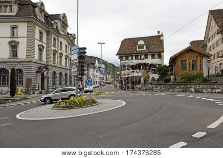 SCHWYZ SWITZERLAND - MAY 09 2016: Roundabout on which goes one car. Buildings and road directional signs and a few people who can be seen in a distance. This is shown on an overcast day.