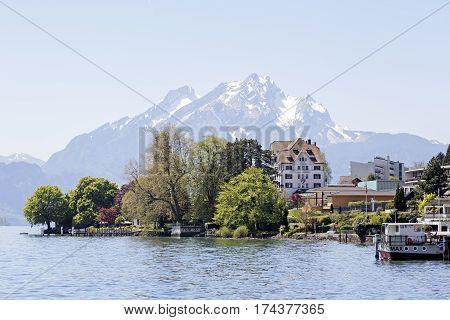 WEGGIS SWITZERLAND - MAY 05 2016: Trees and buildings on the shore of Lake Lucerne and in the distance the snow-capped Mount Pilatus. The scenic area is a popular destination for tourist trips