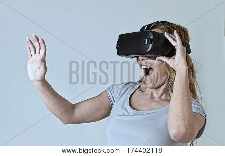 young attractive blond woman wearing headset VR virtual reality vision goggles watching video happy amazed and shocked in new advanced technology experience in gaming concept