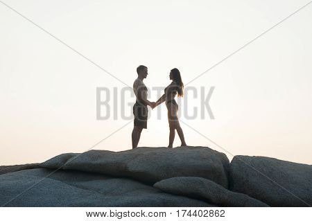 Lovely young adult couple standing on the rocks above tropical sea in isolated.