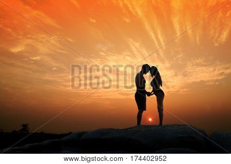 Lovely young adult couple standing on the rocks above tropical sea in Sunset.