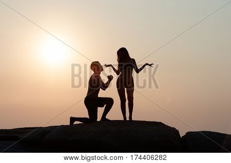 Lovely young adult couple standing on the rocks above tropical sea in Sunset.