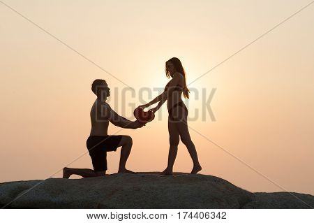Lovely young adult couple standing on the rocks above tropical sea in Sunset.
