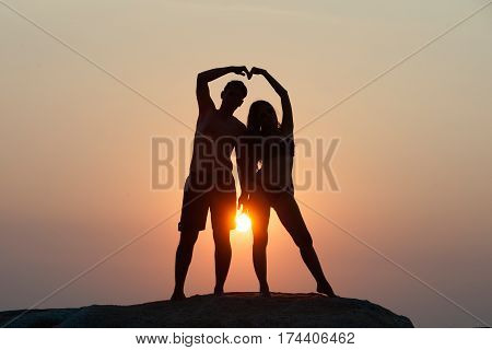 Lovely young adult couple standing on the rocks above tropical sea in Sunset.