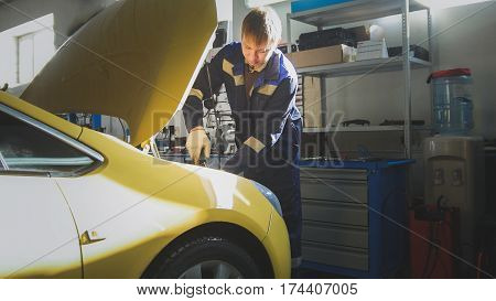 Automobile service - mechanic unscrews detail of car in hood, slider, wide angle
