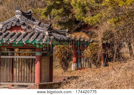Two colorful pagoda style graves sites with traditional tile roofs and oriental designed paint scheme in a wooded area in South Korea