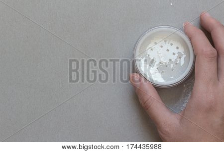 Container with a transparent powder in a female hand in gray background