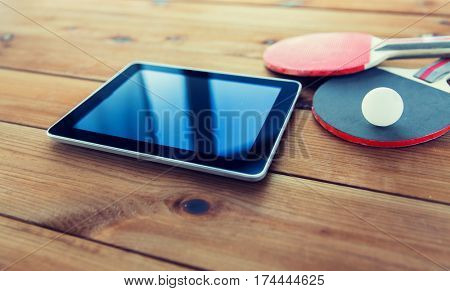 sport, technology, game and objects concept - close up of ping-pong or table tennis rackets with ball and tablet pc computer on wooden floor