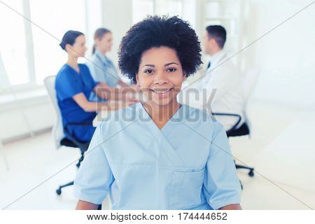 clinic, profession, people and medicine concept - happy african american female doctor or nurse over group of medics meeting at hospital