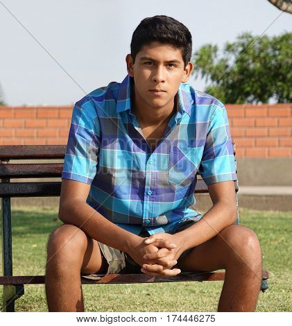 Teen Hispanic Boy Sitting on Public Park Bench