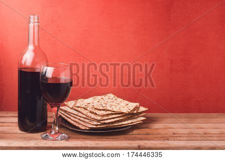 Passover holiday concept with wine glass and matzoh on wooden table over red background