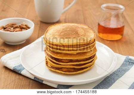 Vegan butternut squash puree pancakes on white plate with maple syrup and pecan nuts. Healthy gluten free breakfast on wooden table