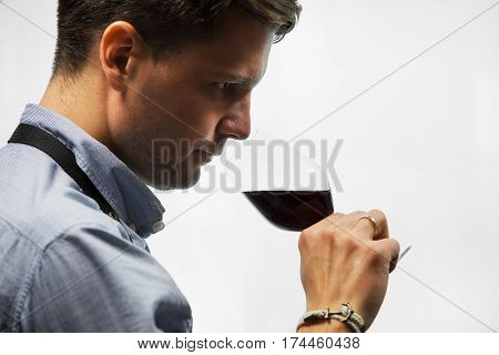 Sommelier smelling flavor of red wine in bokal on white background. Male appreciating color, quality and sediments of drink. Professional degustation expert in winemaking.