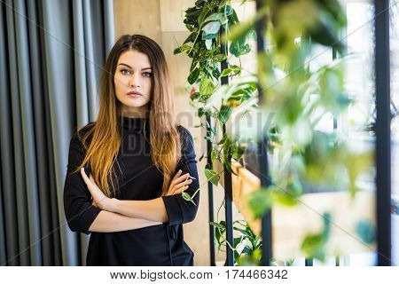 Friendly businesswoman standing with folded arms in a bright neat office looking at the camera
