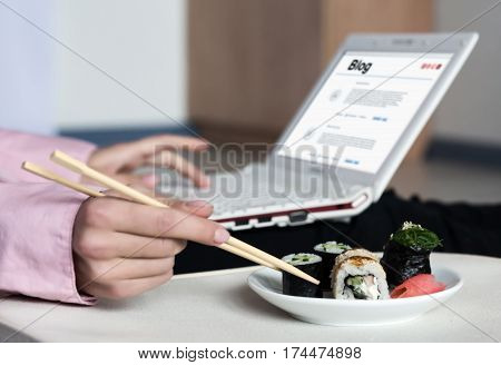 Asian Sushi Set and Woman working on Laptop Computer taking Food Roll with wooden Chopsticks