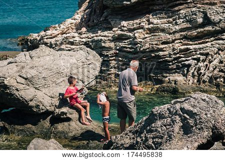 AGHIOS PAVLOS, CRETE, GREECE - JULY 2016: Old man is catching fish together with his young grandsons.
