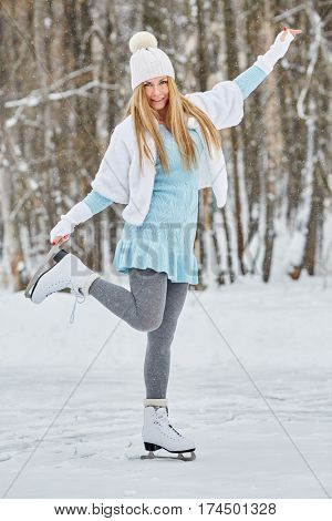 Young woman poses standing on one skate at outdoor skate rink in winter park.