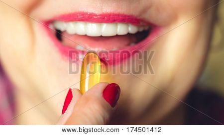 Selective focus close-up of adult woman with beautiful smile holding omega 3 capsule at the mouth