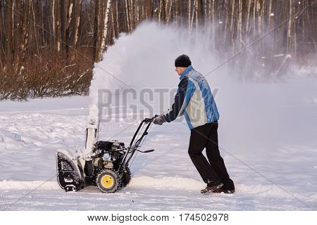 Man removes snow with gas snow thrower at winter day.