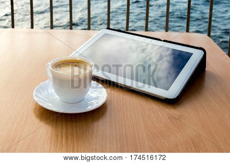 A tablet and a coffee cup on wood table in the sea