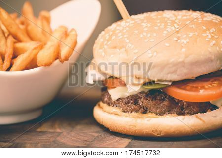 Burger with fresh tomato cheese meat and french fries. Selective focus and toned image