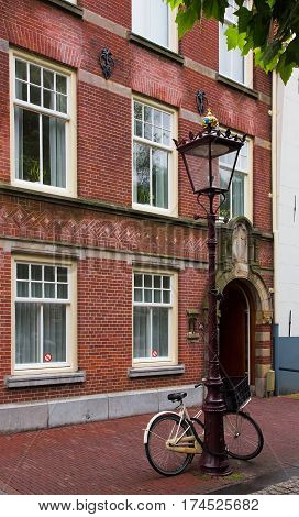 A lone Bicycle parked at a beautiful decorative street lamp on the background of old building facades on a rainy summer day. Amsterdam. Netherlands. Vertical Image