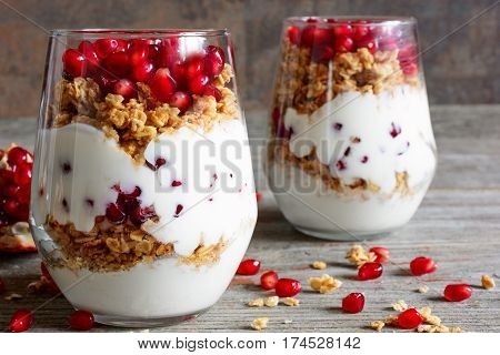 homemade yogurt parfait with granola and pomegranate fruit in glasses on rustic wooden table. healthy breakfast