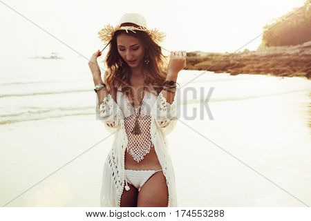 Beautiful boho styled model wearing white crochet swimsuit posing on the beach in sunlight