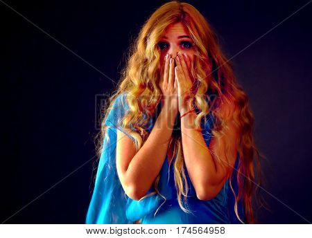 Frightened woman screaming with fear indoor at halloween night. Horror. Girl with tousled long blond hair bawl covered her face on black background.