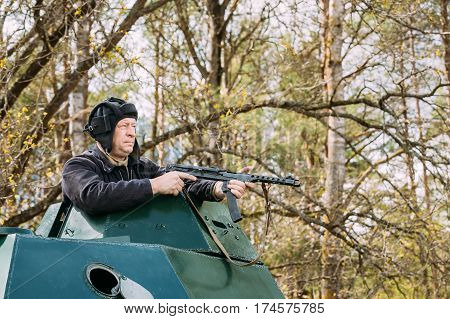 Pribor, Belarus - April 23, 2016: Re-enactor Dressed As Russian Soviet Crew Member Soldier Of World War II Sitting In Armoured Soviet Scout Car BA-64 In Forest And Aiming a Sub-machine Gun at Enemy
