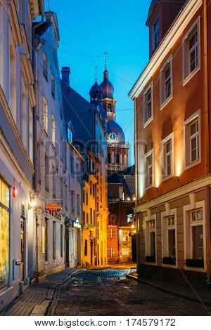 Riga, Latvia - July 1, 2016: View Of Deserted Narrow Cobbled Kramu Street Of Old Town In Bright Evening Illumination With Ancient Architecture Leading To Dome Cathedral Under Summer Blue Sky.