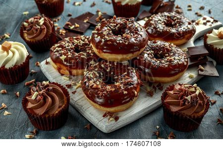 donut rings and vanilla caramel cupcakes with white and dark chocolate chippings and icing served on board.