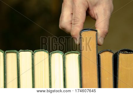 hand of man or woman takes a book on a shalf in the room or library