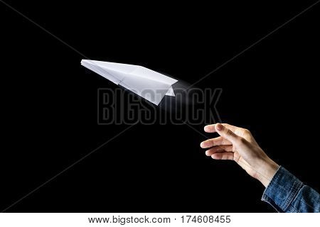 Image of a hand is throwing white paper plane on black background.