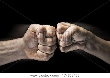 Image close up clash of two fists on black background. Concept of confrontation competition etc.