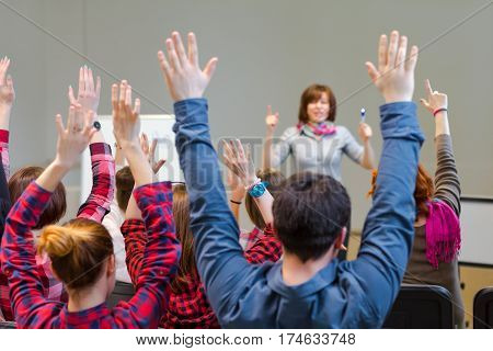Diverse Group of Students in Conference Room raising Arms up actively participating in Seminar Teachers Body on background
