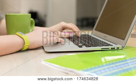 Young female Hands working on modern Laptop Computer close up with green Wristlet on Bangle Coffee Mug and File Folder on wooden Table
