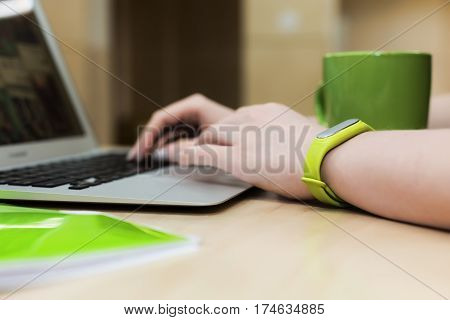 Young female Hands working on modern Laptop Computer close up with green Wristlet on Bangle Coffee Mug and File Folder on wooden Table