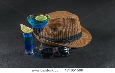 colored drink a combination of blue and green lemon martini glass second drink in shot glass brown sunglasses a brown hat party set