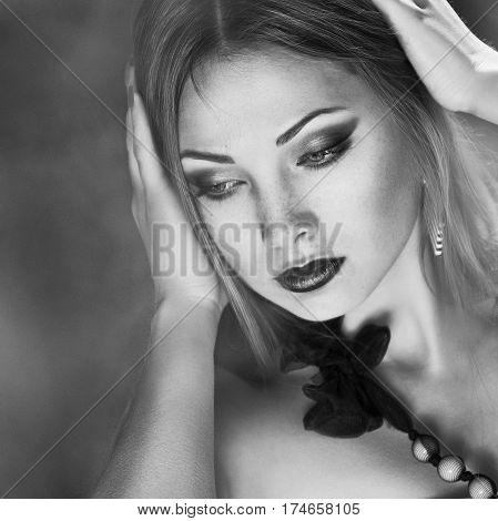 Close-up black and white portrait of sensuality young woman with your hands near the headlong hair a red lips a thoughtful low gaze at the open air in the middle of green blurred leaves at sunny spring day