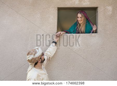 traditionally dressed omani cuple holding hands through a window on an old house