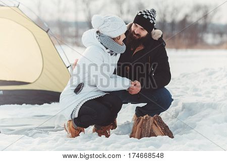 happy couple in warm clothes at winter picnic. bearded boy hold girls hads. concept of the, winter camping, hiking, extream recreation, tourism