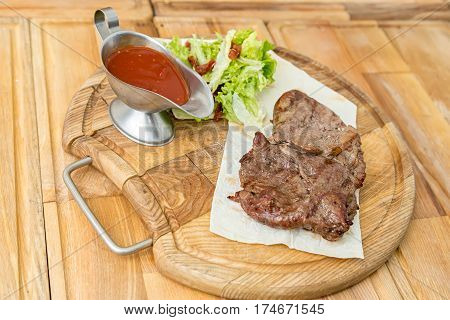 cooked steak on a pita a wooden board standing next to a gravy boat with ketchup and greens