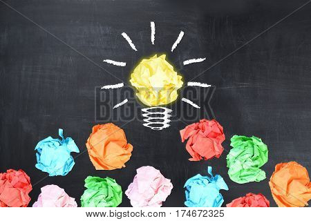 Bright idea concept with light bulb shaped crumpled paper on blackboard
